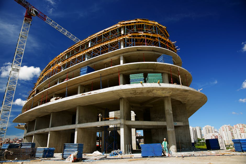 Low angle view of a circular building under construction with a crane, clear blue sky