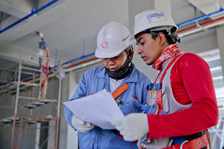 Two engineers in safety helmets reviewing construction plans at a worksite