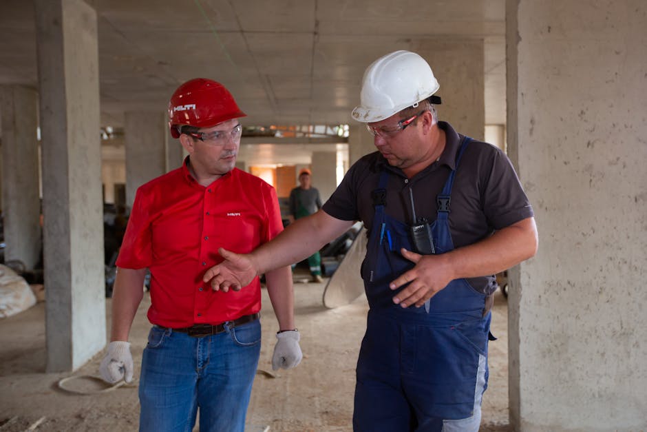 Two construction workers in safety gear discussing plans at a construction site