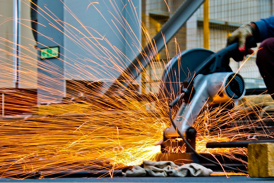 A worker operates a grinder cutting metal, creating a vibrant display of sparks in an industrial setting